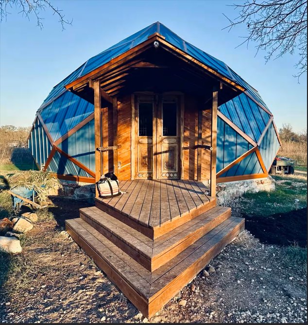 Geodesic temple with a blue metal roof, wooden doors, and a timber porch