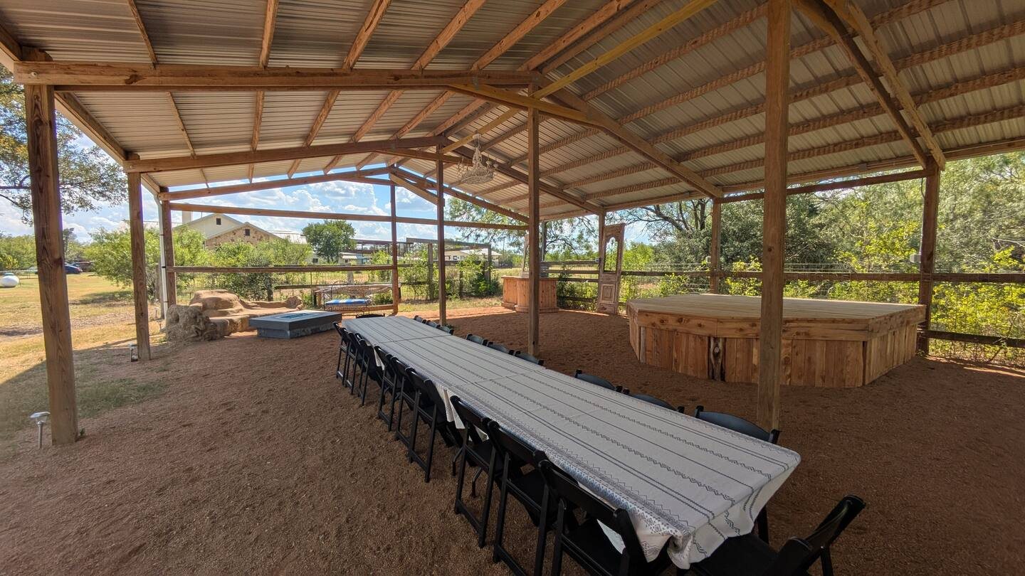 Covered pavilion with a long table and a timber stage under a metal roof