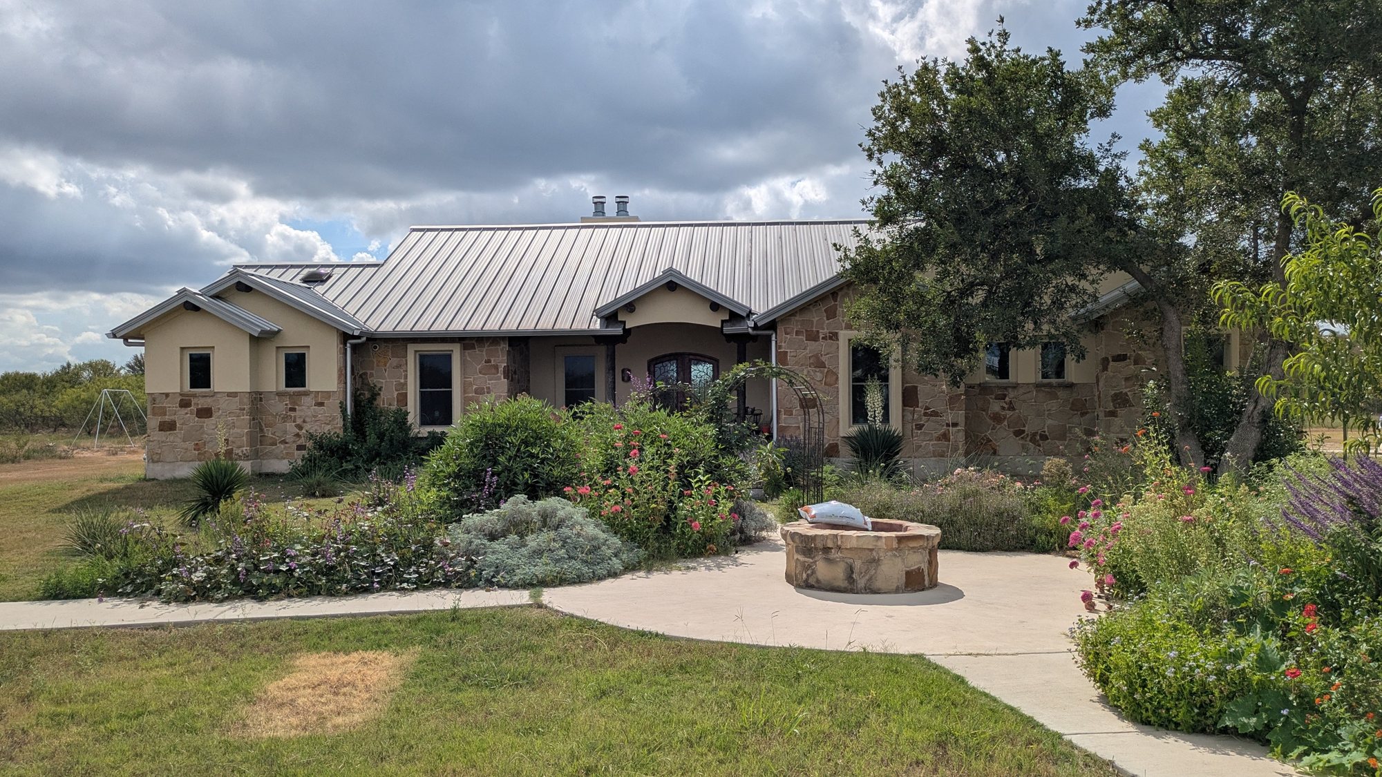 Stone ranch house with a metal roof, garden, and round fire pit